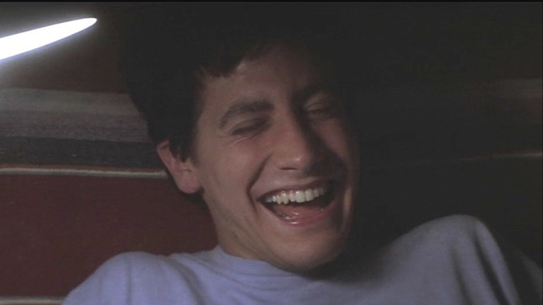 Jake Gyllenhaal as Donnie Darko sitting in bed and laughing