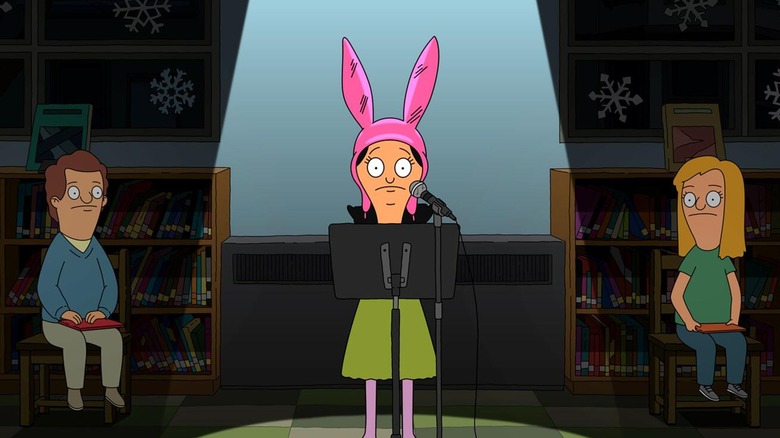 Louise stands at a microphone and music stand in spotlight