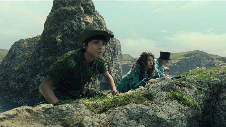 Peter Pan and the Darling children peer over a rock in Peter Pan & Wendy