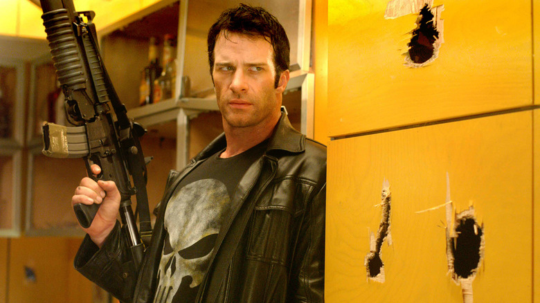 Thomas Jane as The Punisher, holding a gun next to a damaged wall