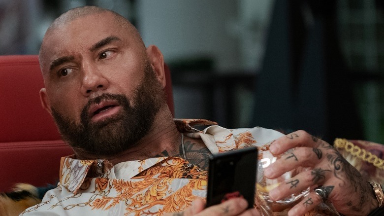 Dave Bautista leaning over holding phone Glass Onion