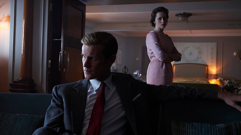 Matt Smith's Philip sits on a couch, staring to his right while in the background, over his left shoulder, Claire Foy's Queen Elizabeth stands with her arms crossed (The Crown)