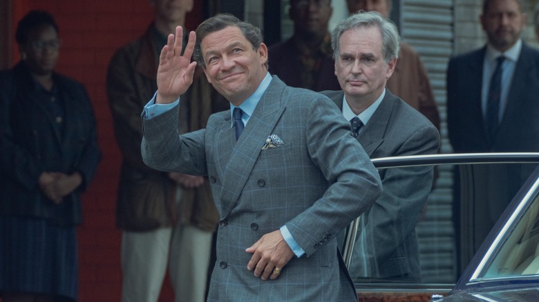 Dominic West's Prince Charles, exiting a car, waves while several people stand behind him in The Crown