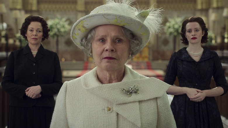 Olivia Colman's and Claire Foy's versions of Queen Elizabeth II stand behind her on either side dressed in black, while the version played by Imelda Staunton is foregrounded, dressed in white (The Crown)