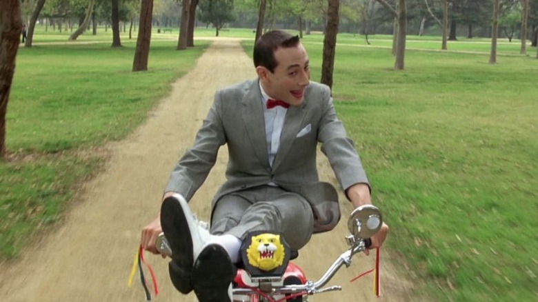 Pee-Wee riding bike with his legs on the handlebars
