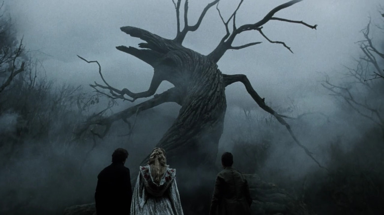 Three figures stand in front of a twisted tree