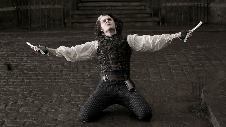 Sweeney Todd kneeling with arms outstretched, holding razorblades