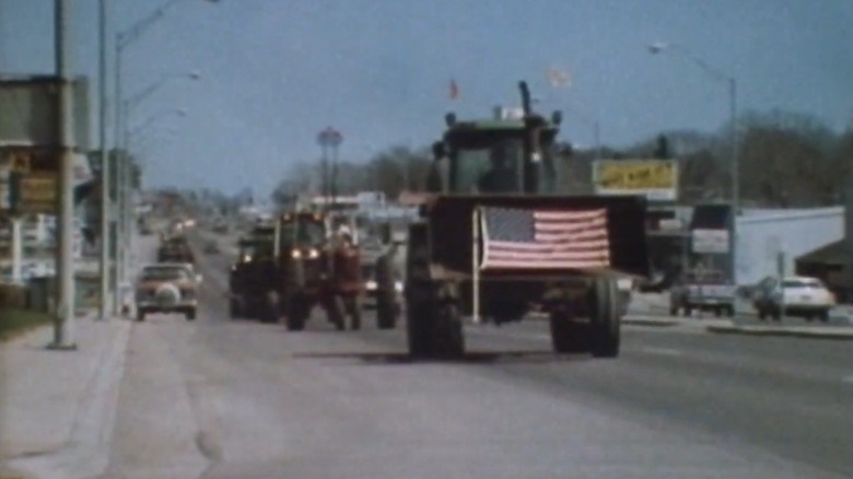 A tractor with an American flag on the front drives down the road in Down and Out in America