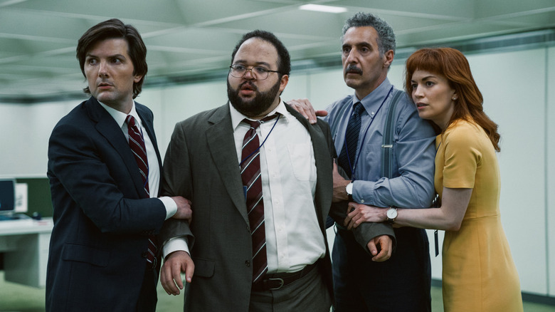 Adam Scott as Mark S., Zach Cherry as Dylan G., John Turturro as Irving B., and Britt Lower as Helly R. holding onto each other for support in season 1 of Severance