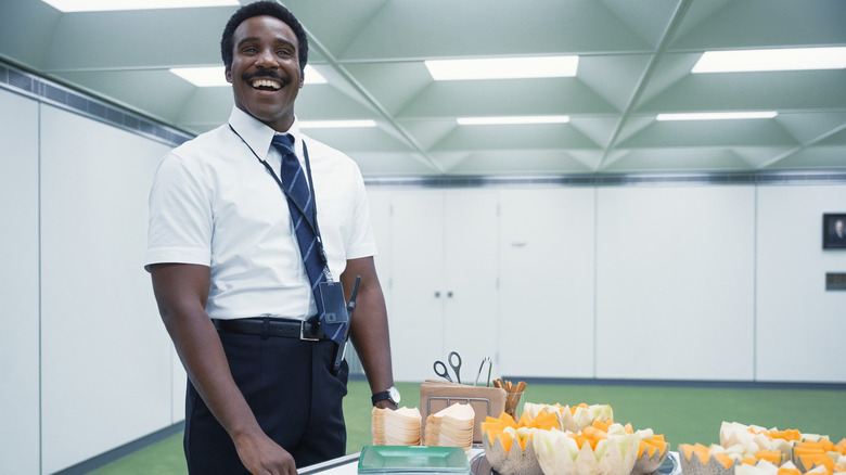 Tramell Tillman as Mr. Milchick with a broad smile as he wheels in a cart of office snacks in Severance season 1