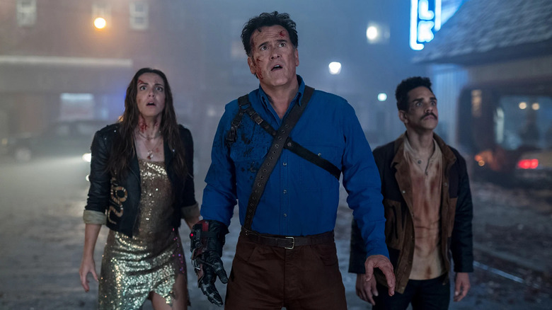 Ash flanked by two friends in a dusty street at night in Ash against Evil Dead