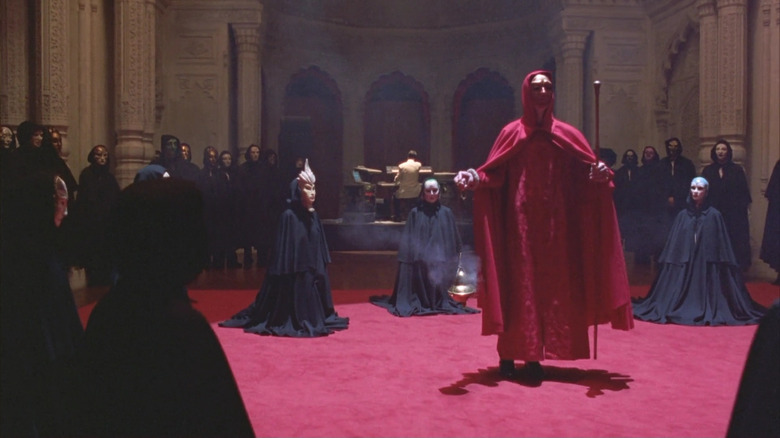 A circle of masked men wearing black robes, with one in red at the center, in Eyes Wide Shut (1999)