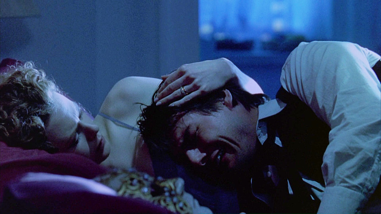 Tom Cruise as Bill Harford crying, held by his wife Alice Harford (Nicole Kidman), with a mask on the pillow next to them, in Eyes Wide Shut