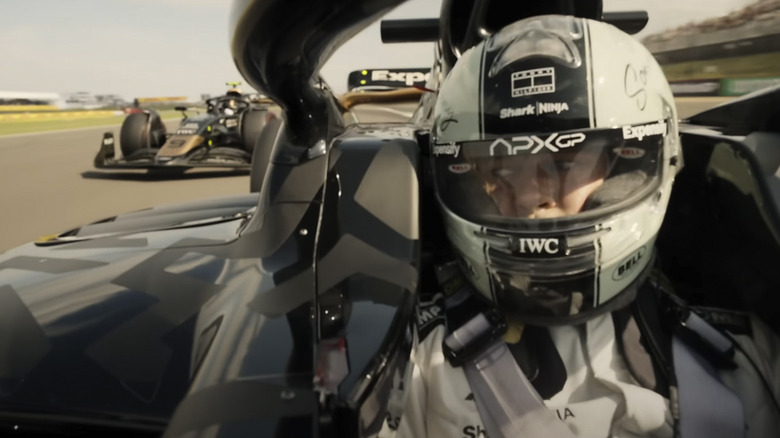 Sonny Hayes in an F1 racecar glances over his shoulder to see another car gaining on him on the track in F1