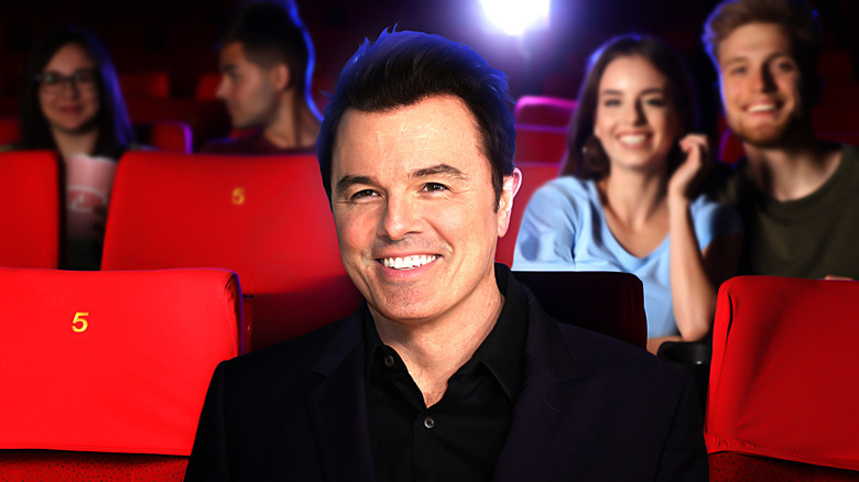 Um sorridente Seth MacFarlane sentado em uma sala de cinema com outros espectadores espalhados atrás dele