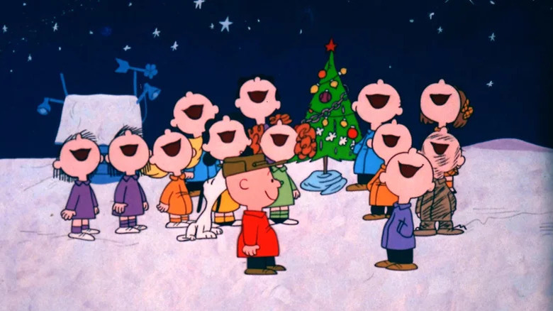 Charlie Brown surrounded by friends singing around the Christmas tree