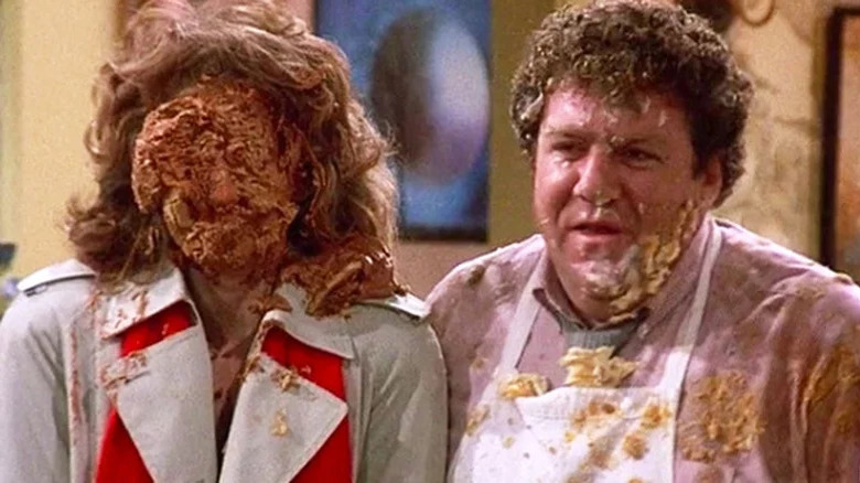 Vera from Cheers standing next to Norm with a pie in her face