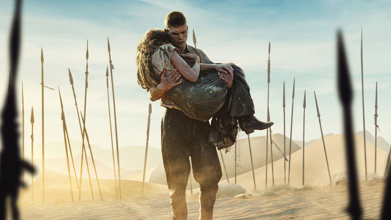 Rand carrying a woman in sand filled with upright spears in the Wheel of Time season 3 poster