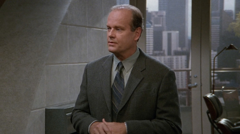 Frasier stands in his apartment wearing a suit