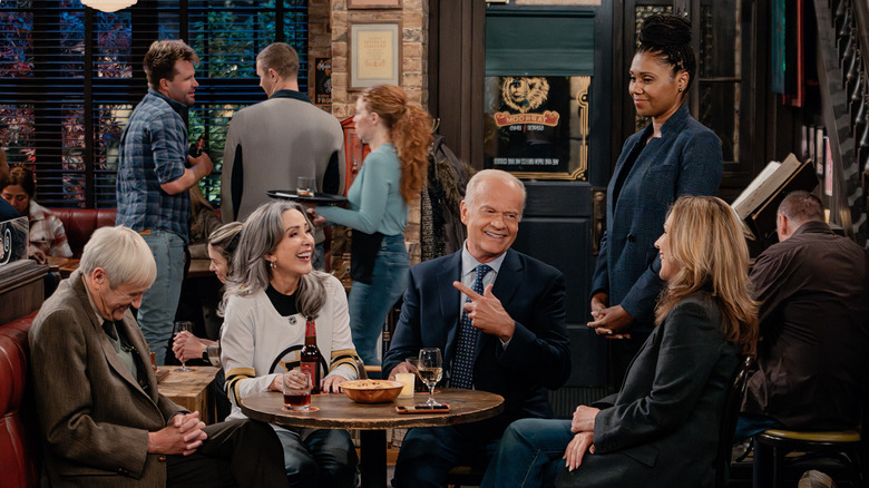 Frasier, Alan, Holly, and Ross all sit around a table at a bar while Olivia stands next to the table