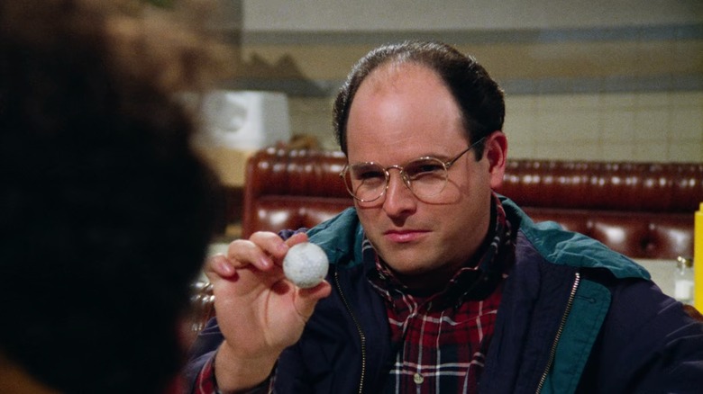 Jason Alexander's George triumpantly holds up a golf ball at the diner in Seinfeld