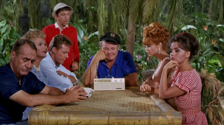 The castaways of Gilligan's Island sitting around a table listening to a radio on Gilligan's Island