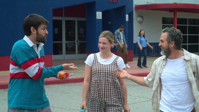 Cooper Raiff and Lili Reinhart as young Hal & Harper, talking excitedly with Mark Ruffalo as their father