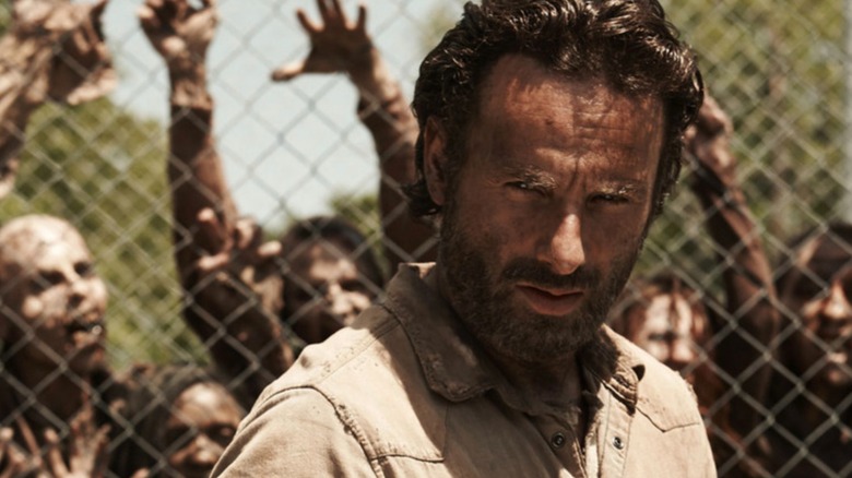 Rick Grimes em pé na frente de uma cerca com zumbis atrás dela em The Walking Dead