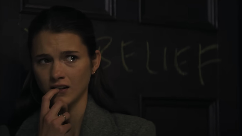 Chloe East as Sister Paxton teary-eyed in front of a door labeled 'Belief' in Heretic