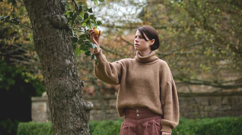 Jessie Buckley picking fruit from a tree in Men