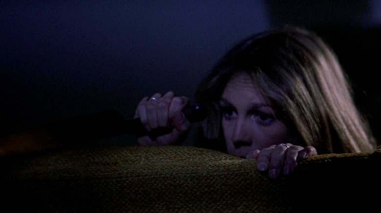 Jamie Lee Curtis hides on the couch with Michael Myers in Halloween.
