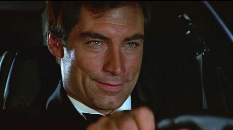 Timothy Dalton's James Bond smiles as he sits behind the steering wheel of a car in The Living Daylights