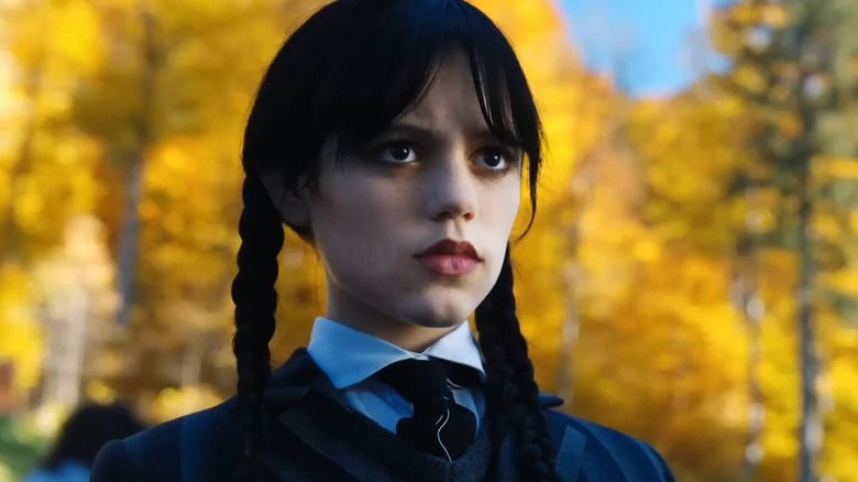 Wednesday Addams na frente da folhagem de outono olhando