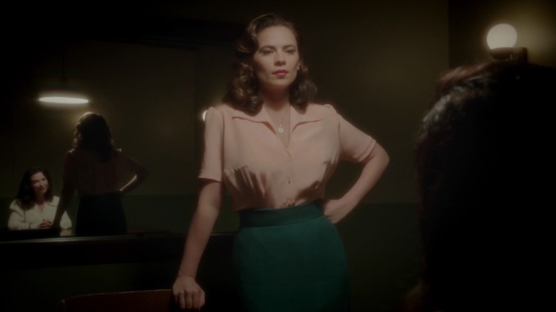 Agent Carter dressed in a pink blouse and stands in the Carter Agent's questioning room