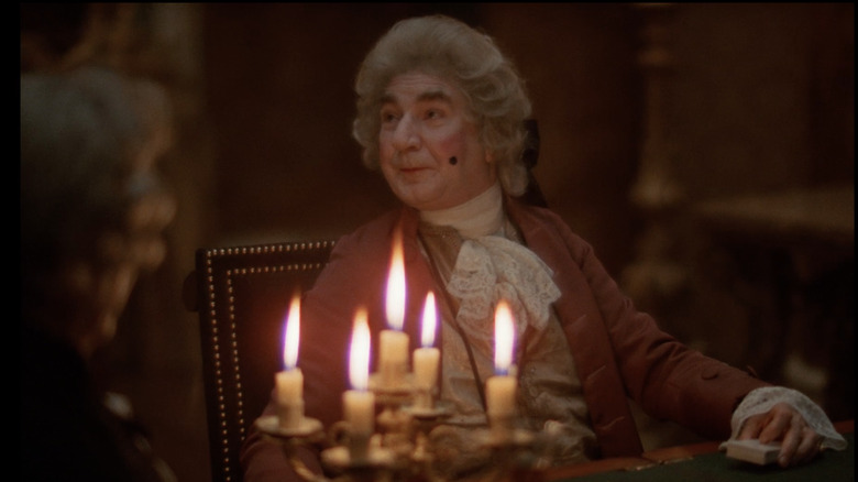 Candles illuminate a man in a white powdered wig and stark make-up
