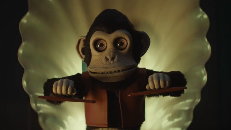 A scary monkey toy holding drumsticks in The Monkey