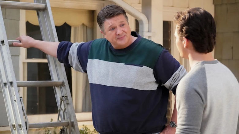 Lance Barber as George Cooper Sr. leans on a ladder and chats with Montana Jordan as Georgie Cooper in Young Sheldon