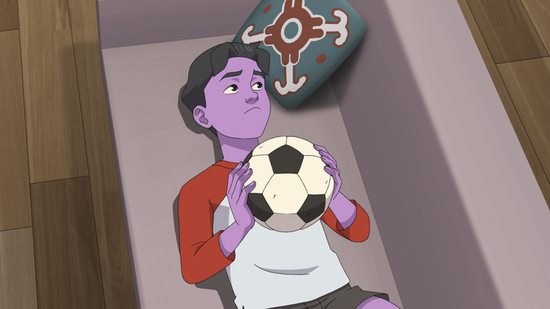 Oliver holds a football ball while lying on the couch in invincible