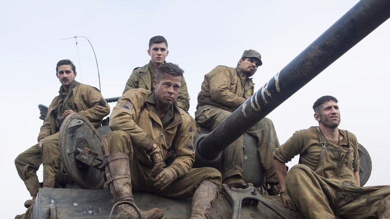 Boyd, Don, Norman,Trini, Grady sit on top of a dirty army tank with serious expressions in Fury