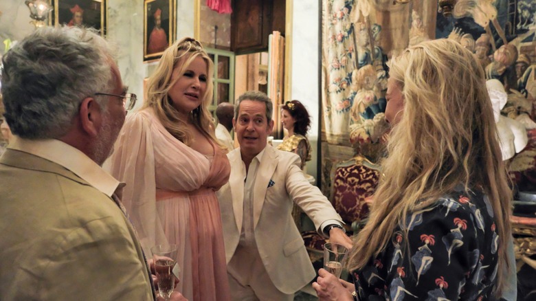 Tom Hollander's Quentin introduces Jennifer Coolidge's Tanya to two people who are facing away from camera, all standing in an ornately decorated room, in The White Lotus