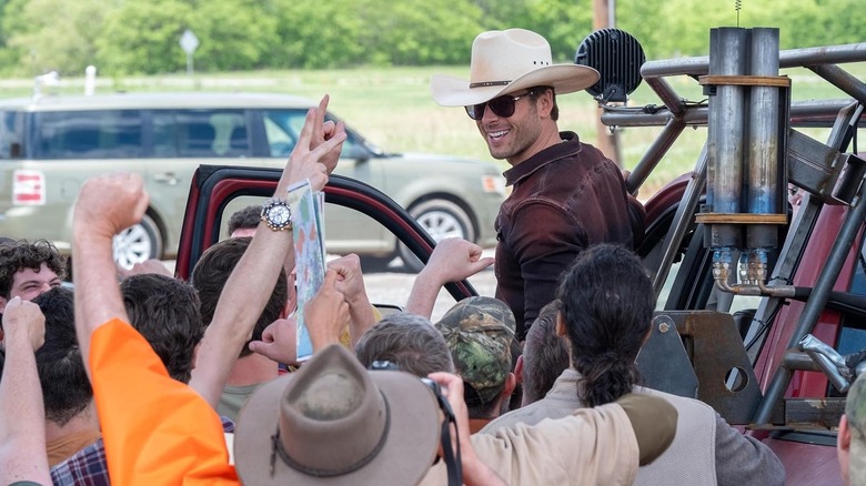 Tyler Owens sorrindo em seu chapéu de cowboy, cercado por pessoas, em Twisters