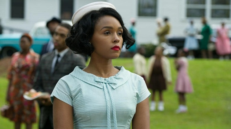 janelle monae in a 50s dress and hat on the grass with people in the background in the movie hidden figures