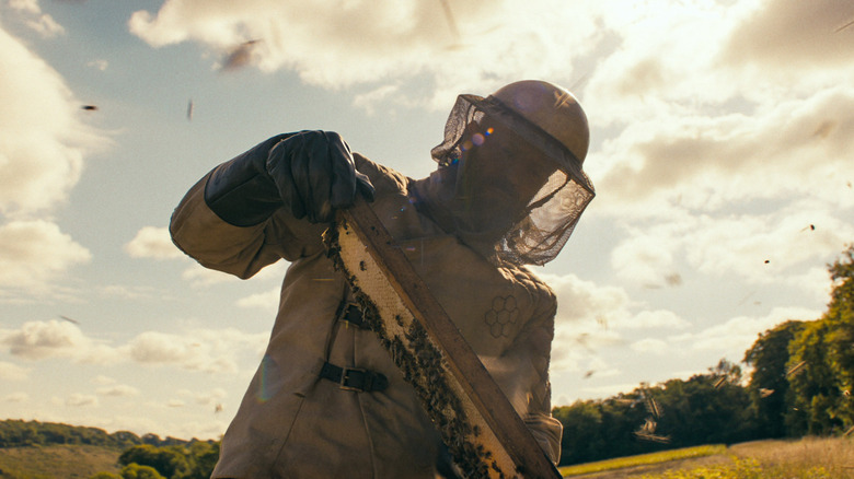 Adam Clay in a beekeeper suit holding a panel full of bees in The Beekeeper