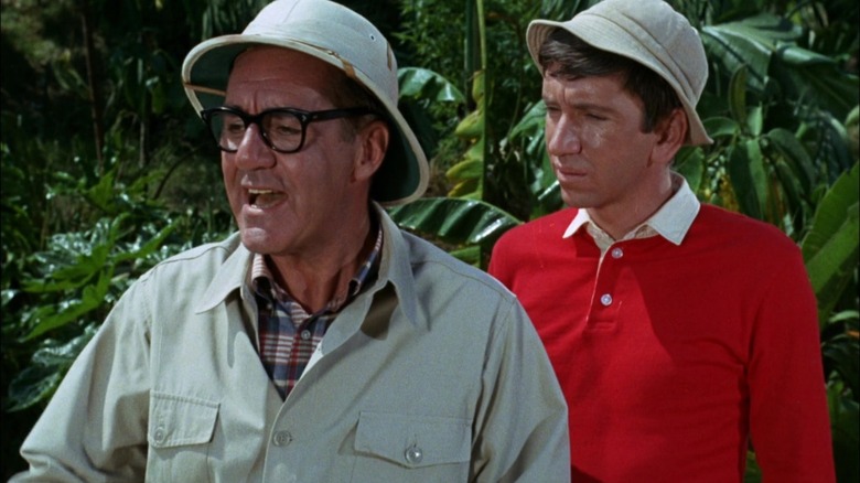 El Sr. Howell usa un casco y gafas con Gilligan detrás de él en la isla de Gilligan.