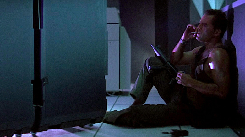 Bruce Willis smokes a cigarette while hiding behind cubicles in Die Hard