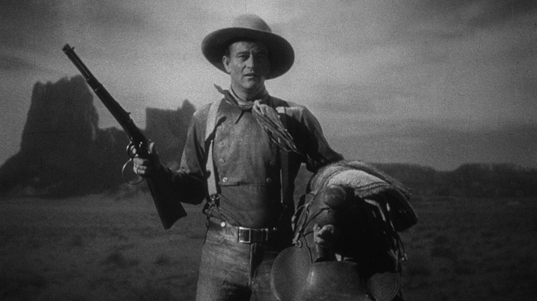 John Wayne holding a rifle and saddle in Stagecoach