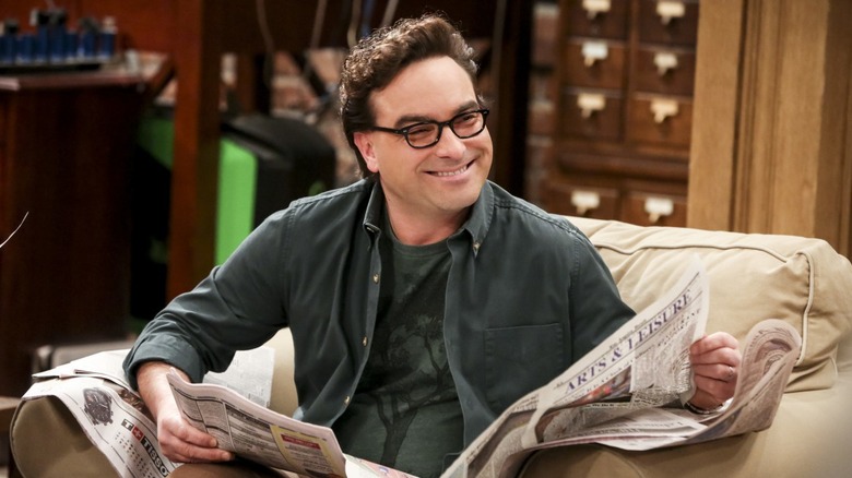 Leonard reading a newspaper on an armchair and grinning on The Big Bang Theory