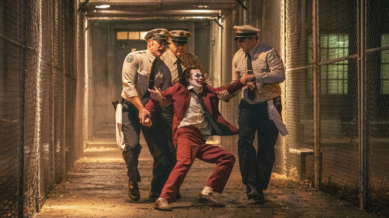 Brendan Gleeson as correction officer Jackie Sullivan watching Joaquin Phoenix's Arthur Fleck dragged through a prison courtyard in Joker: Folie à Deux