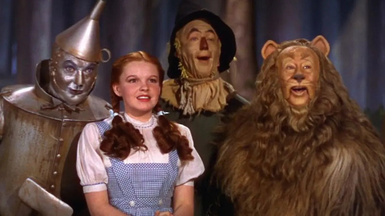 The Tin Woodman, the Scarecrow, Dorothy, and the Cowardly Lion, looking happy in The Wizard of Oz