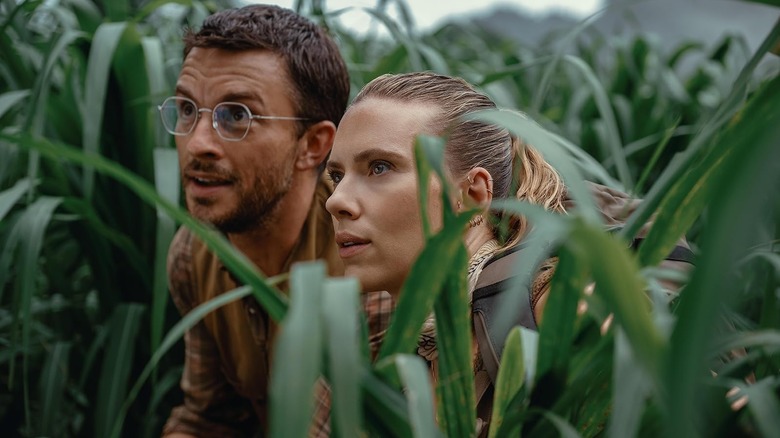 Jonathan Bailey as Henry Loomis and Scarlett Johansson as Zora Bennett crouching in the tall grass in Jurassic World Rebirth